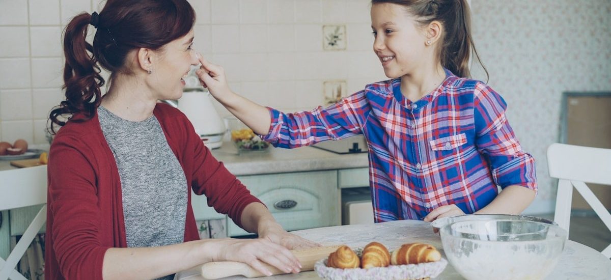 Young mother and her cute daughter have fun smearing nose each other with flour while cooking together in the kitchen on holidays. Family, food, home and people concept