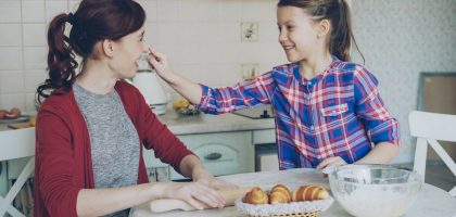 Young mother and her cute daughter have fun smearing nose each other with flour while cooking together in the kitchen on holidays. Family, food, home and people concept