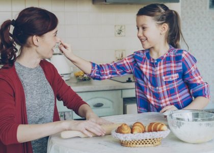 Young mother and her cute daughter have fun smearing nose each other with flour while cooking together in the kitchen on holidays. Family, food, home and people concept